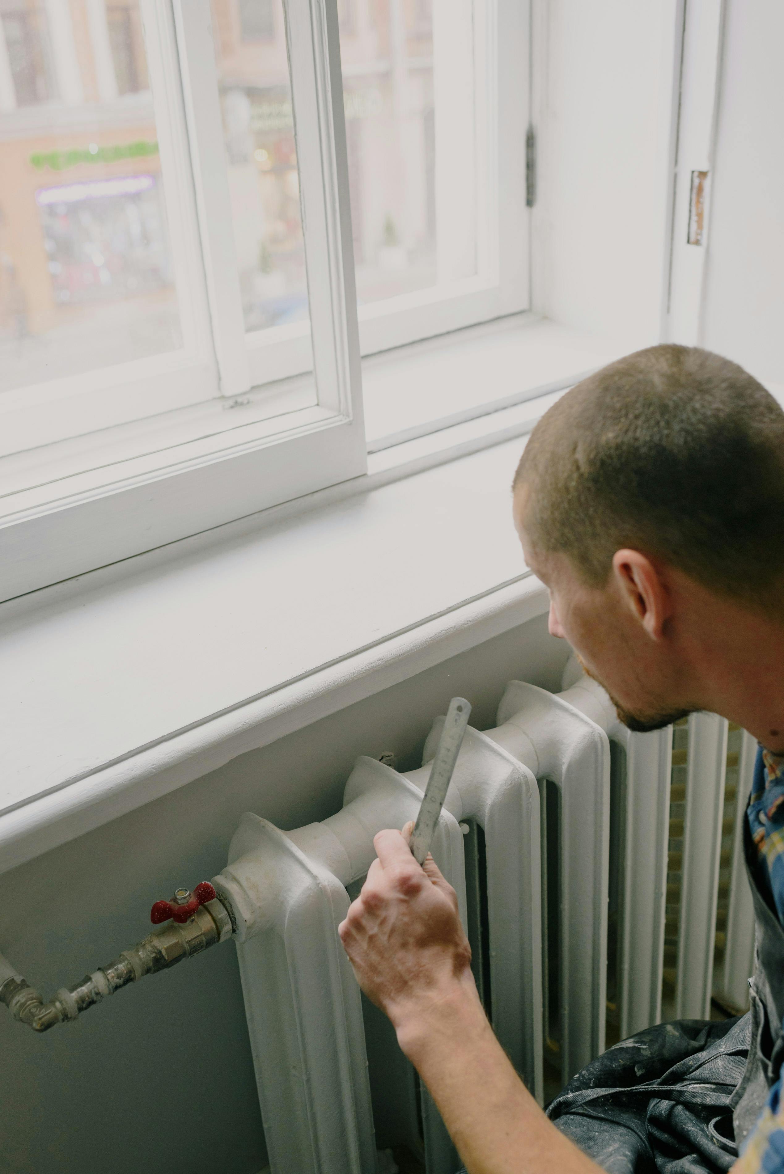 Technicien ajustant un radiateur près d'une fenêtre.