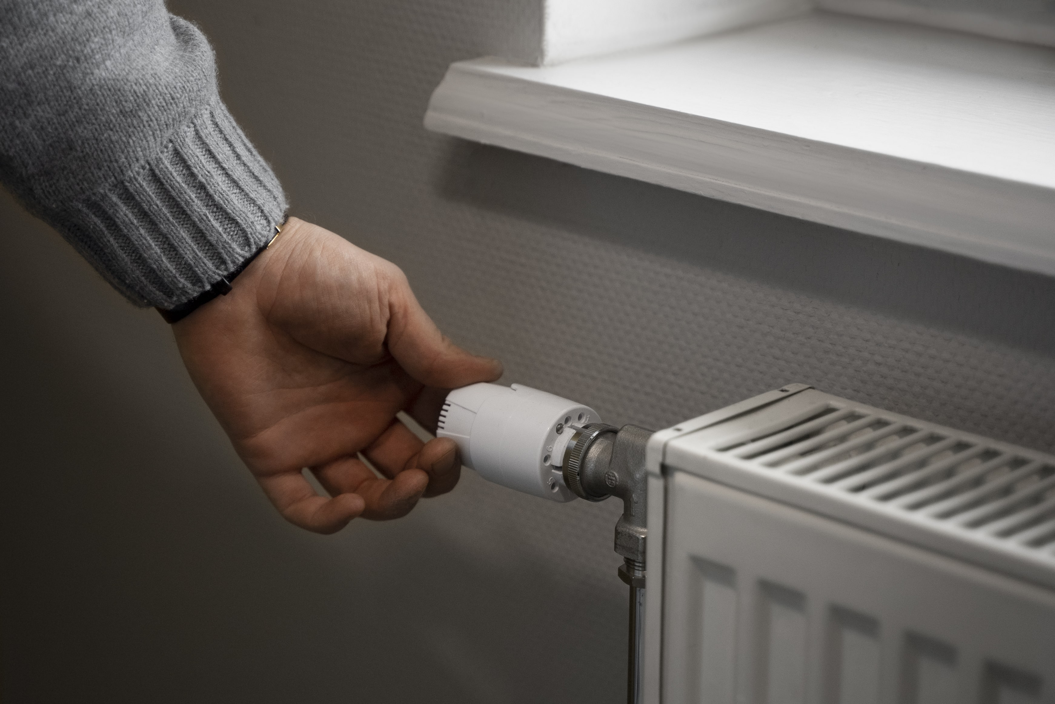 Main ajustant un thermostat sur un radiateur sous une fenêtre.